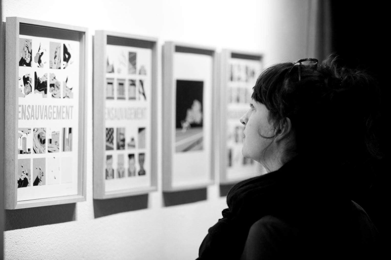 Une visiteuse devant les œuvres encadrées de l'exposition Ensauvagement